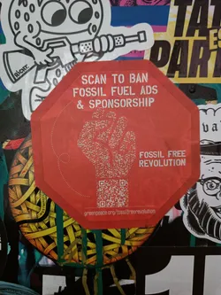 Street sticker A red octagonal sticker with a QR code and the text 'Scan to ban fossil fuel ads & sponsorship' and 'Fossil free revolution'. The QR code leads to greenpeace.org/fossilfreerevolution