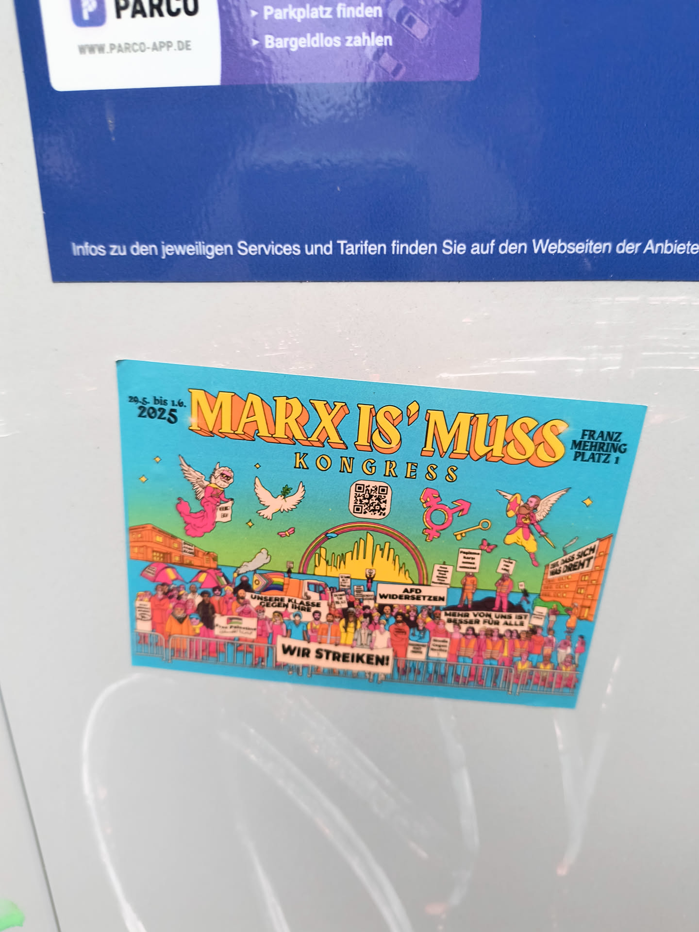The sticker is rectangular with a bright blue background. At the top, in large, yellow, 3D-style lettering, it reads 'MARX IS' MUSS'. Below this, in smaller yellow letters, it says 'KONGRESS'. To the left, '29.5. bis 1.6. 2025' is written in white. The central imagery depicts a diverse crowd of people holding signs, with tents and buildings in the background. A rainbow arch spans across the scene. There are symbolic elements like a winged figure holding a sign, a dove with an olive branch, a transgender symbol, and a key. A QR code is visible on the right side of the 'KONGRESS' text. The overall style is colorful and illustrative, reminiscent of political posters.
