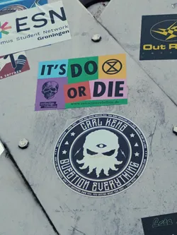 A round sticker featuring a stylized octopus with one eye, surrounded by text that reads "Carl Keno" and "Question Everything". The background is dark gray/black with white text and imagery. The style is dark, edgy, and graphic. 