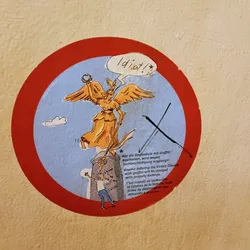 Street sticker This is a round sticker with a red border and a light blue center.  The main image is a caricature of the Victory Column with a winged figure seemingly being defaced by a smaller figure. The text warns against graffiti and vandalism with messages in German, English, and French. 