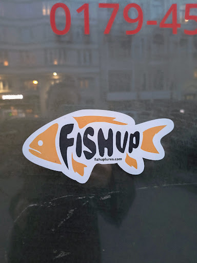 A die-cut sticker of a fish with the text "FISHUP" and "fishluplures.com". The fish shape is outlined in orange, with the text filling the body of the fish.