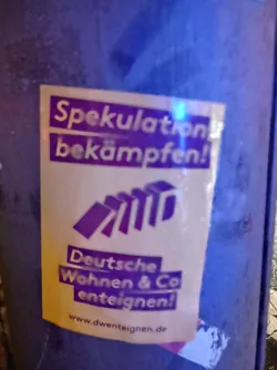 Street sticker A sticker advocating for the expropriation of Deutsche Wohnen & Co. The sticker features the text "Spekulation bekämpfen!" (Fight Speculation!) and "Deutsche Wohnen & Co enteignen!" (Expropriate Deutsche Wohnen & Co!), along with a graphic of falling dominoes, symbolizing the impact of speculation.  A website address is also included.