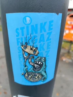 Street sticker A sticker featuring a cartoon monster devouring a broken skateboard on a light blue background. The word "STINKE FUNGAZ" is repeated vertically on the sticker. There is a logo in a circle at the top left corner.