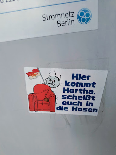 Street sticker This sticker shows a cartoon drawing featuring a red armchair and a nervous, sweating character with a Hertha BSC flag. It contains the text "Hier kommt Hertha, scheißt euch in die Hosen", which roughly translates to "Here comes Hertha, shit your pants".