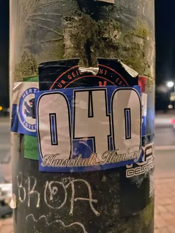 A sticker with the number 040 and the text "Hansestadt Hamburg" on a pole.  There are other stickers around it.