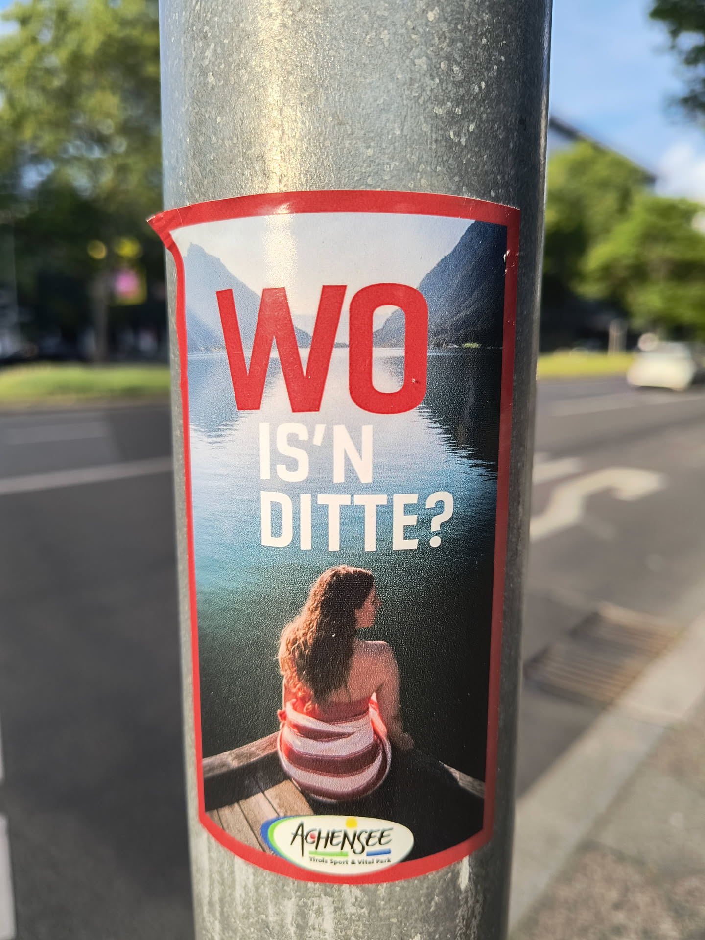 A rectangular sticker with a red border, featuring a scenic view of Achensee, Tirol, with a woman sitting on a pier in the foreground. The text 'Wo is'n Ditte?' is prominently displayed in red and white. The Achensee logo is at the bottom.