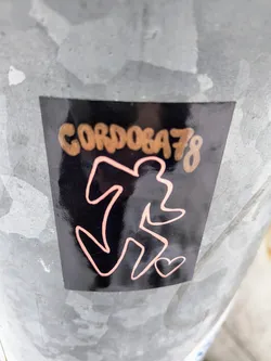 Street sticker A black sticker with rose gold text and design. The text says "Cordoba78" and the design is an abstract figure with a small heart. The sticker is affixed to a metallic surface.