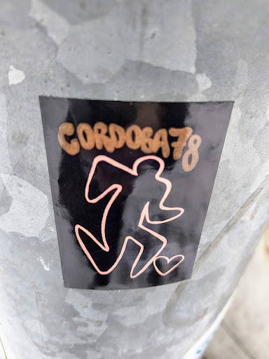 A black sticker with rose gold text and design. The text says "Cordoba78" and the design is an abstract figure with a small heart. The sticker is affixed to a metallic surface.