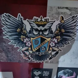 Street sticker A sticker featuring an illustration of an owl wearing a crown and large wings.  The owl is positioned on a coat of arms style shield with a hop, stars, and a floppy disk.  The text below reads "Vincit qui se vincit".