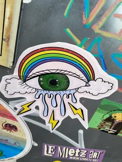 Trippy sticker featuring a mystical eye peeking from a cloud with a rainbow above, and lightnings and tears below. 