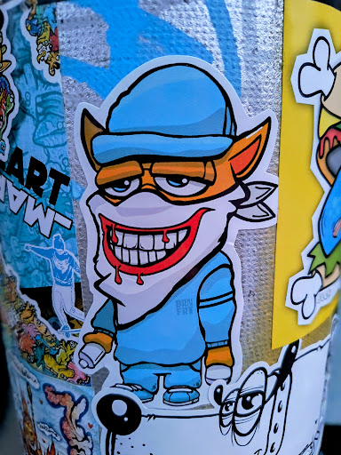 Street sticker A sticker featuring a cartoon fox character with a large, toothy smile and dripping blood, wearing a blue cap and matching outfit. The art style is reminiscent of graffiti and street art. It is among various other stickers.