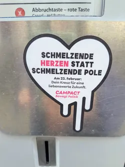 Street sticker The sticker is heart-shaped with black and white colors, except for the word 'Herzen' which is in pink. The heart shape is slightly melted at the bottom. The text on the sticker says, 'Schmelzende Herzen statt schmelzende Pole. Am 23. Februar: Dein Kreuz für eine liebenswerte Zukunft.' at the top, and 'Campact. Bewegt Politik' at the bottom.