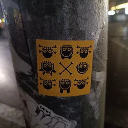 A yellow square sticker with a grid of cute, spooky black characters.  Some have crossbones, others have rounded bodies.  A simple, eye-catching design.