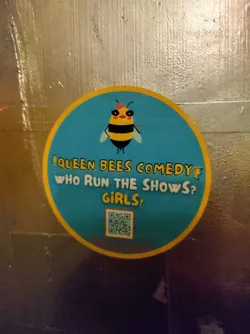 Street sticker Round sticker featuring a cartoon bee and the text "Queen Bees Comedy. Who run the shows? Girls!"  It includes a QR code at the bottom.