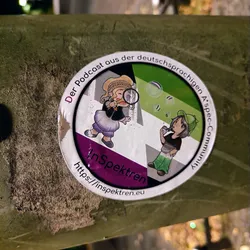 Round sticker featuring two cartoon characters, one with a magnifying glass and the other blowing bubbles. The sticker includes the podcast name 'In Spektren' and its website URL.  The design uses colors associated with the asexual spectrum.