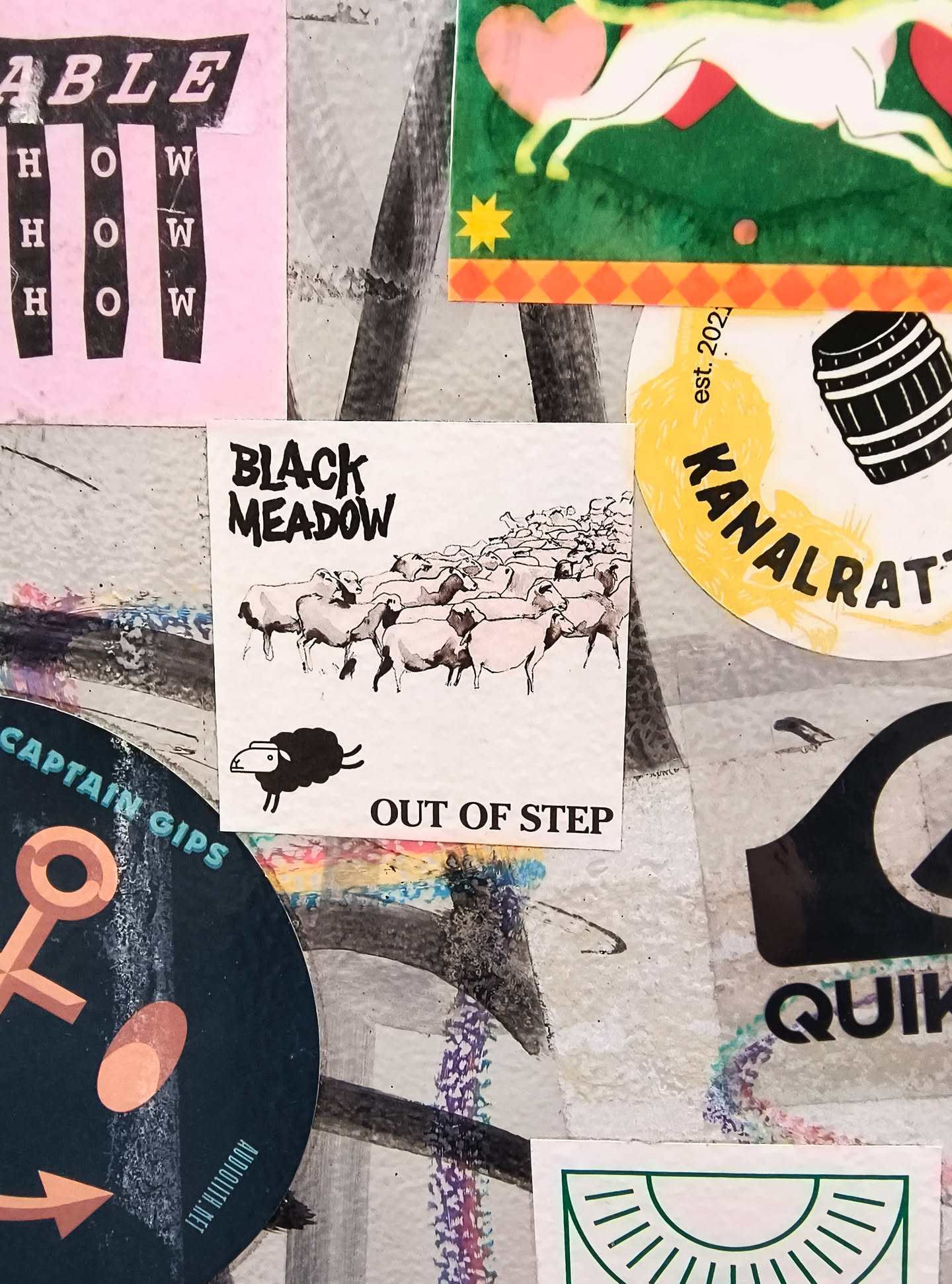 The sticker is square-shaped with a white background. It features a black and white illustration of a flock of sheep walking towards the right. In the foreground, a single black sheep with a white face is facing left, appearing to be separate from the flock. Above the illustration, the text 'BLACK MEADOW' is written in a distressed, bold font. Below the illustration, the text 'OUT OF STEP' is written in a simpler, sans-serif font.