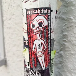 Street sticker A sticker featuring a stylized skull character in red and white. The character has a humanoid body and is depicted in a confident pose.  The sticker has a black border with the artist's Instagram handle, @rekah.tatu, at the top. There is text along the sides, possibly in Japanese or a similar East Asian script. The art style is bold and graphic.