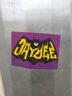 Street sticker A purple sticker featuring a stylized Batman bat silhouette with the word "DAYZEE" written in yellow across it.  The Batman image is reminiscent of classic 1960s Batman illustrations. 