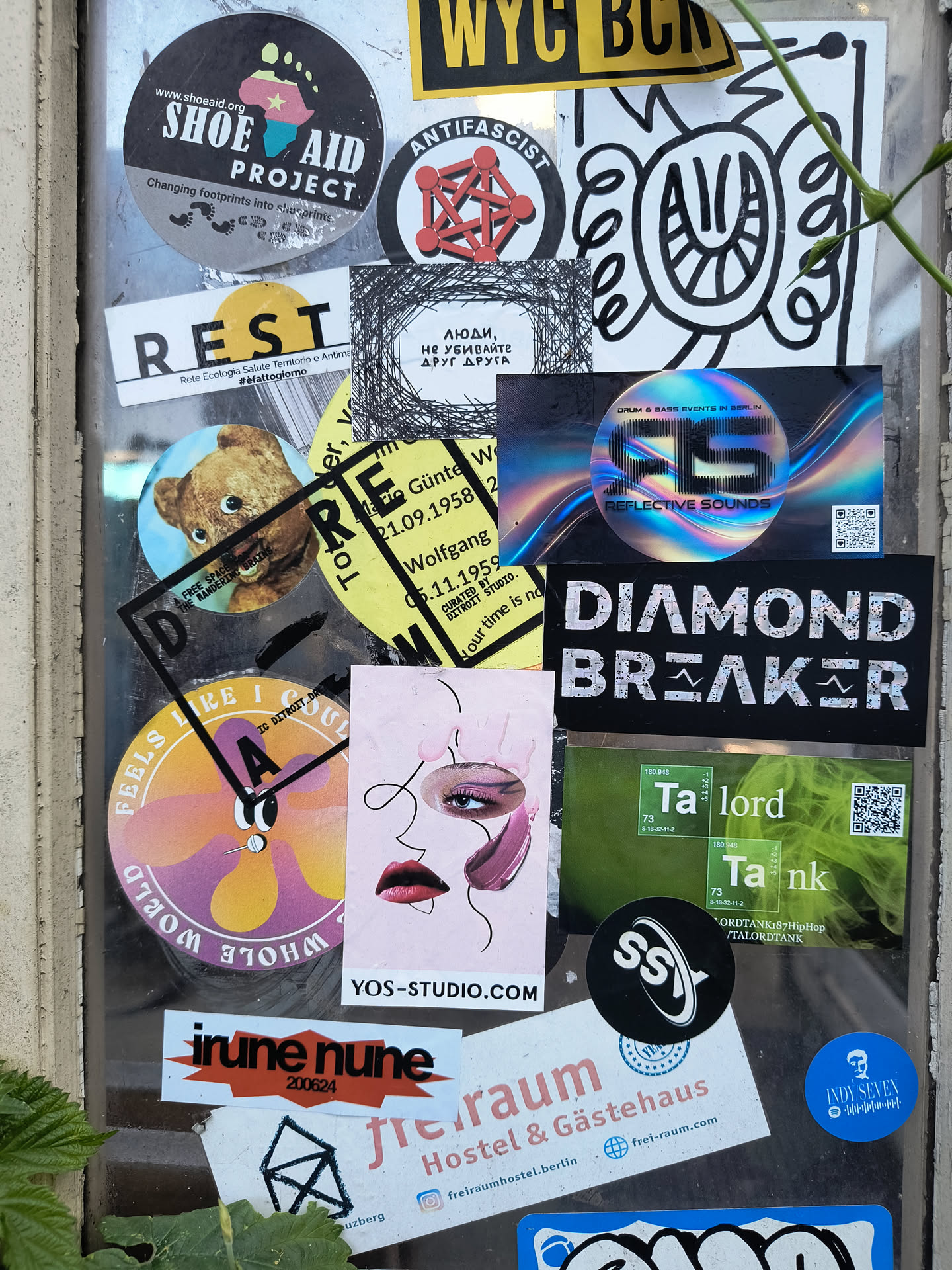 A window with various stickers. The central sticker features a stylized drawing of a face with artistic makeup and the text "YOS-STUDIO.COM".