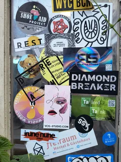 Street sticker A window with various stickers. The central sticker features a stylized drawing of a face with artistic makeup and the text "YOS-STUDIO.COM".