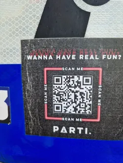 Street sticker A black sticker with a QR code in the center and the text 'Wanna have real fun?' on top. The text 'PARTI.' is at the bottom. The QR code is surrounded by a red square and the words 'SCAN ME' on each side and below.