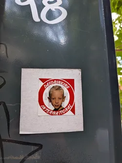 Street sticker Square sticker with a central red circular emblem. Inside is a photo of a young boy against a red and white striped background with faint beer glass icons. The text 'DAYDRINKING INTERNATIONAL' wraps around the circle.