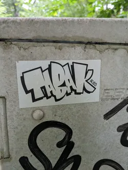 A rectangular sticker with black and white graffiti art. The word ThaBak is written in a stylized bubble letter font. In the bottom right corner, there is a small text that says ACID3.