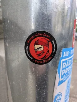 A round sticker with a black background and a red design. It features a person wearing a red balaclava with the word "VALPE" written on it. The sticker also contains the text "Sempre al tuo fianco - Biaucorosso - Appartenenza - Curva Filatoio".
