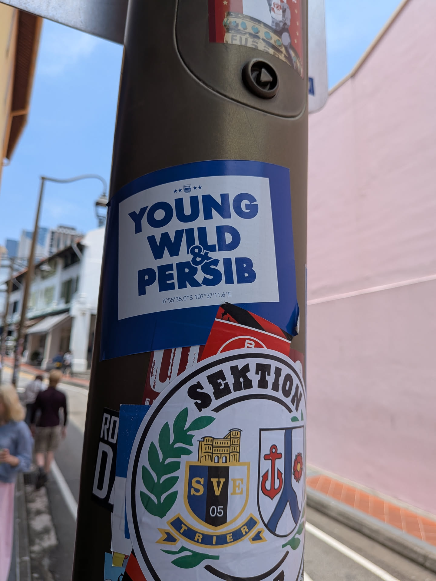 A rectangular sticker with a blue border and white center. It displays the bold blue text 'YOUNG WILD & PERSIB' stacked vertically, topped by five stars and a small logo, with geographic coordinates printed at the bottom.