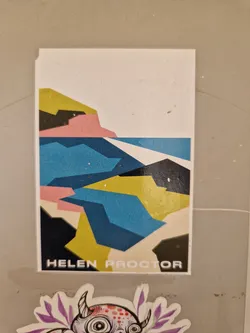 A sticker featuring an abstract landscape design by artist Helen Proctor. The artwork is primarily composed of geometric shapes in blue, yellow, pink, and black, suggesting a stylized coastal scene. The artist's name is printed at the bottom.