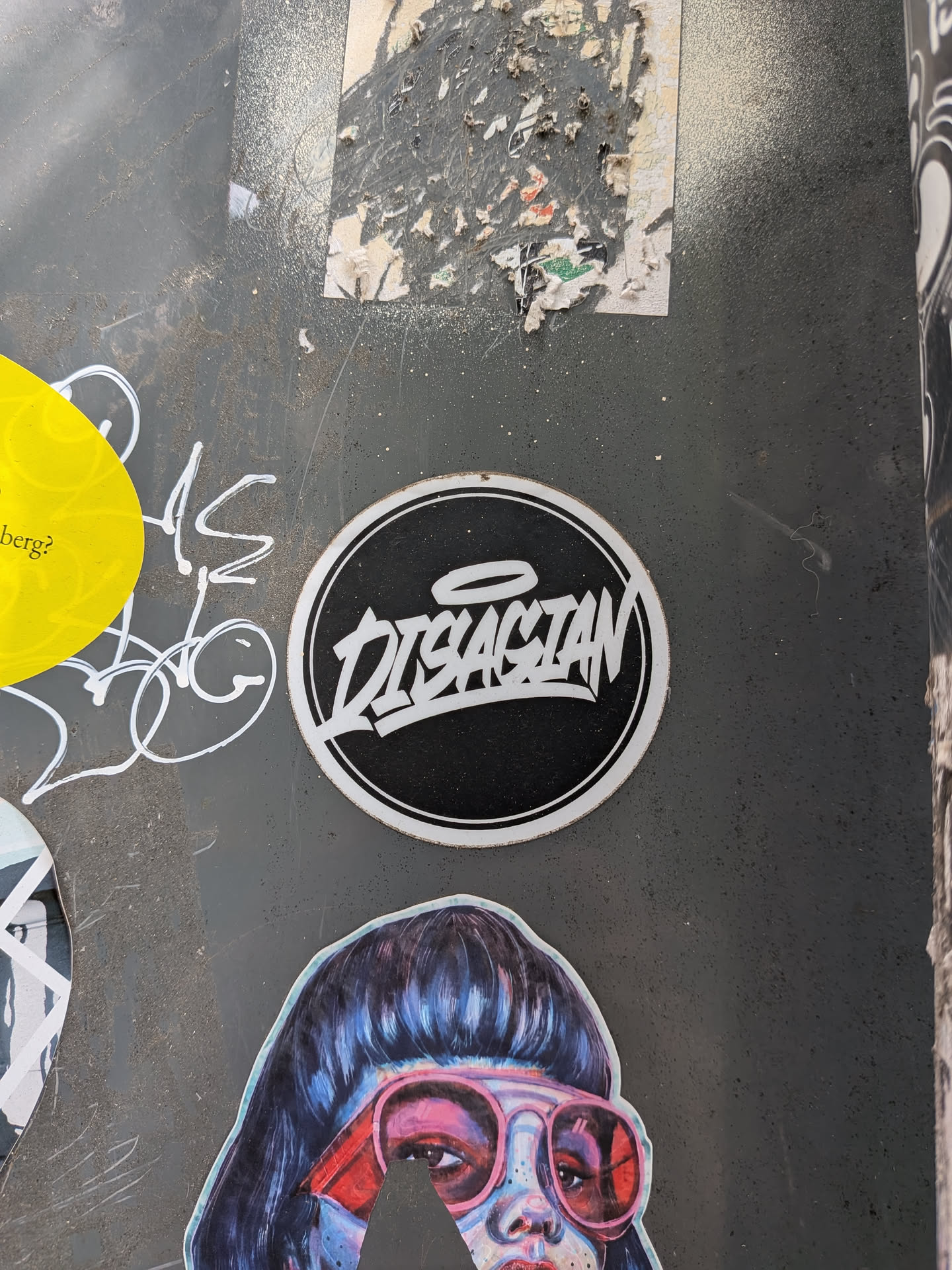 A round black sticker with a white double-ring border. The center features the word 'DISASTAN' in a sharp, white graffiti-style font, accented by a small halo above the letters.