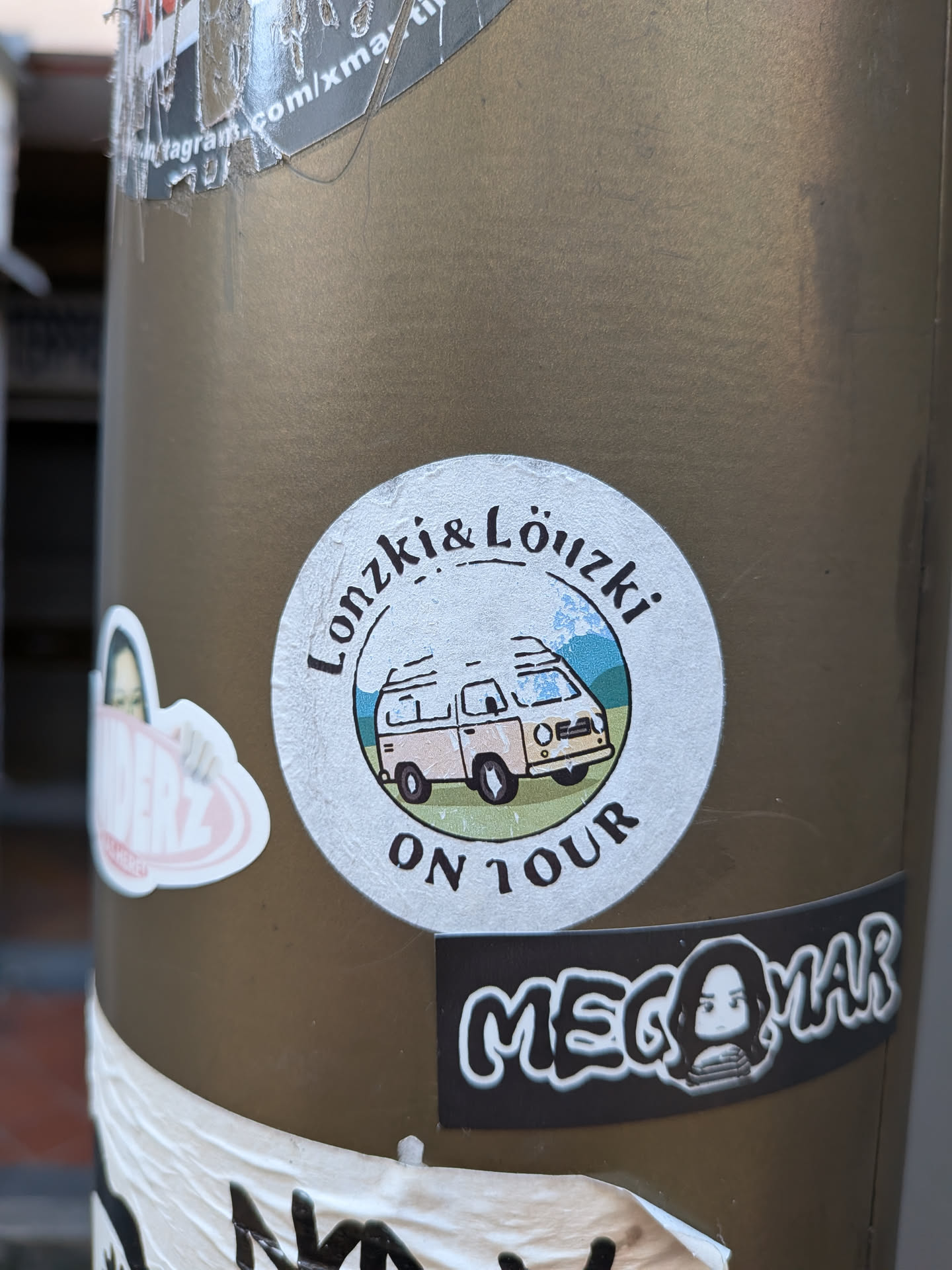 A round sticker showing a cartoon camper van in a mountain landscape, with text reading 'Lonzki & Löuzki ON TOUR'.