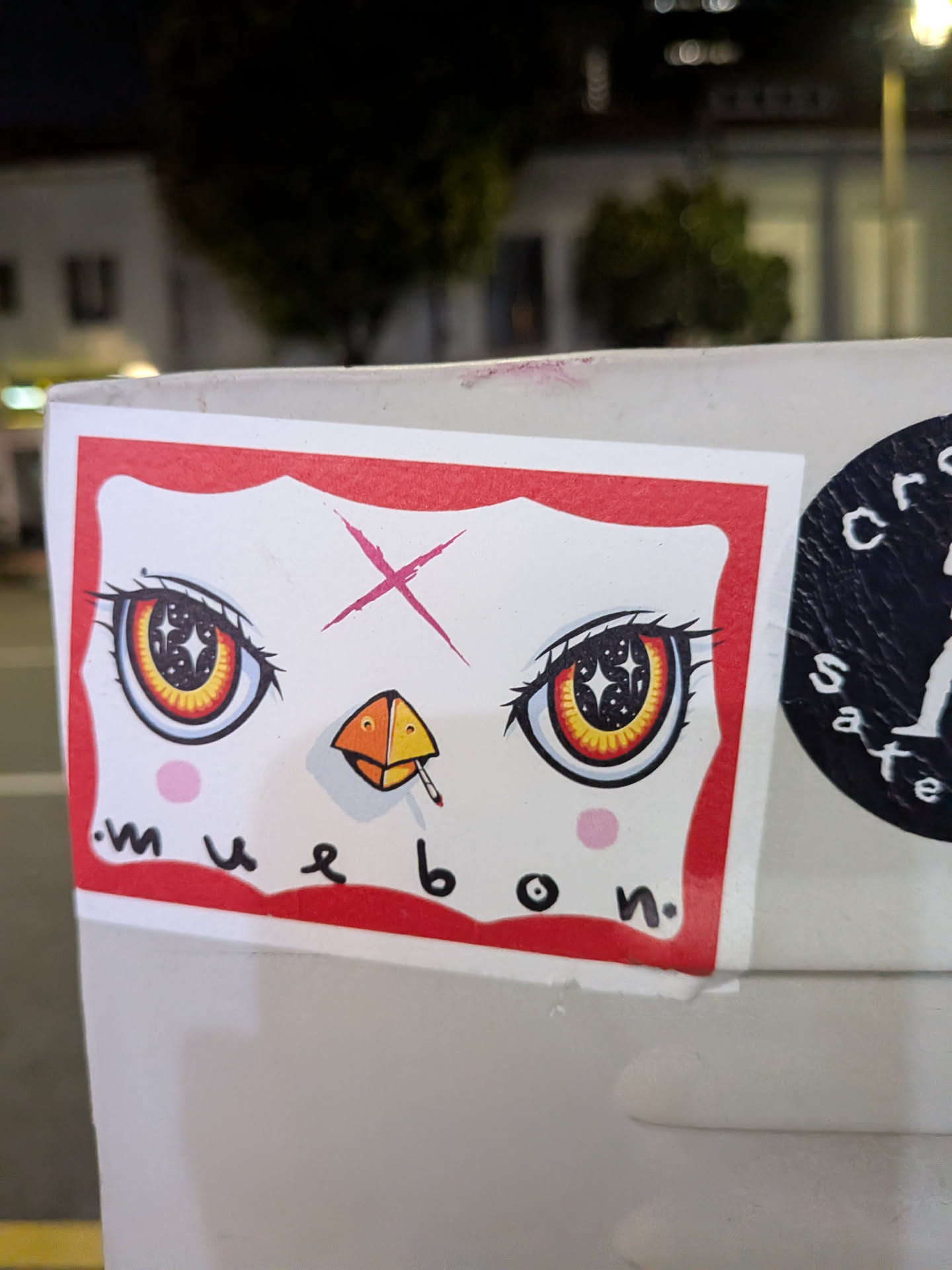 Rectangular sticker with a red border depicting a white face. Features large anime eyes with starry pupils, a pink forehead 'X', a smoking beak, and the text 'muebon' at the bottom.