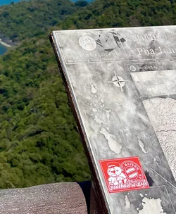 Street sticker The sticker is a vibrant red square with white details. It features a cartoon character, likely a mascot, wearing a red uniform with a matching hat and white accents. To the right of the character is the iconic circular logo of FC Bayern München, rendered in red and white, with the letters 'FC BAYERN E.V.' encircling the Bavarian flag pattern. Below the character and logo, in a stylized white script, are the words 'Football is Life'. The sticker has clean edges and appears to be adhered to a weathered informational sign.