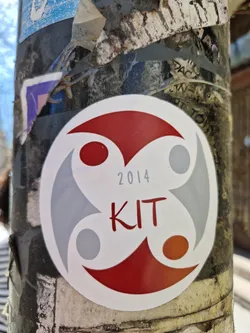 Street sticker A round sticker with a logo featuring three stylized shapes in grey and red, reminiscent of a stylized human form. The year 2014 and the abbreviation KIT are printed in the center.