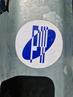 Street sticker A round sticker with a blue and white logo. The logo features a stylized letter 'P' or similar form within an oval shape, accompanied by parallel lines.  The sticker appears to be affixed to a metallic surface.