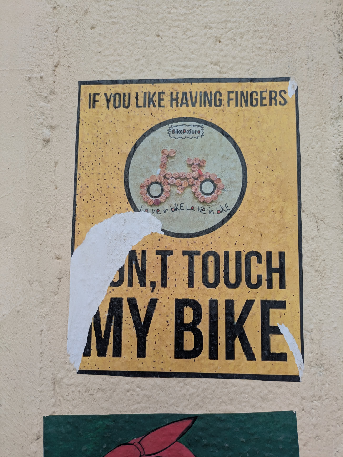 The sticker, featuring a bicycle made of flowers, carries a clear warning against touching the bike. The message is bold and direct. It is partially torn.