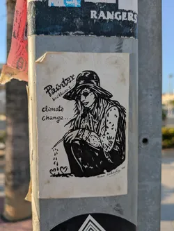 Street sticker A sticker shows a black and white drawing of a painter wearing a hat, holding a brush, and sitting down. The words "Painter brilliant... climate change..." are written on the sticker. It's signed 'Juan Salcedo, 20'.
