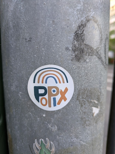 This sticker is on a gray pole. The sticker has a semi-circle rainbow at the top, with arcs of brown, beige and dark blue. Below the rainbow, the sticker reads "PPlx" with the "PP" in dark blue, "l" in beige and "x" in brown.