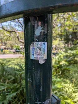A square holographic sticker with an iridescent finish. It displays an Instagram QR code with the platform's logo in the center and the handle '@JOAO_TATTOO' printed at the bottom.