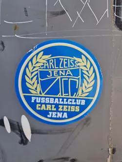 A round sticker featuring the logo of FC Carl Zeiss Jena, a German football club. The logo is predominantly blue and yellow, with text that says  'Carl Zeiss Jena' and 'Fussballclub Carl Zeiss Jena'.
