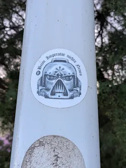 Street sticker A circular white sticker featuring a grayscale illustration of a Space Marine helmet. The helmet has 'BADAB' written on the cheek. Arched gothic text above reads 'Beim Imperator nichts Neues' next to a Spotify logo.