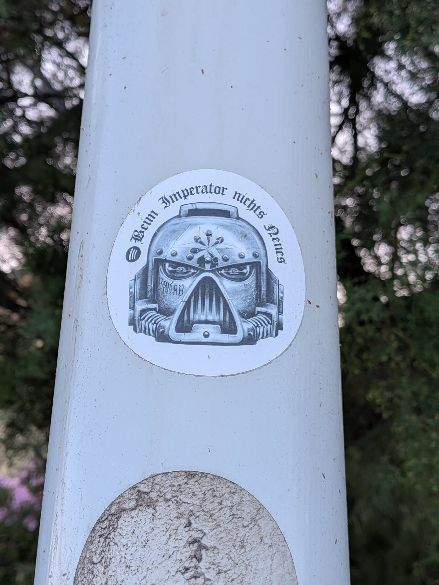 A circular white sticker featuring a grayscale illustration of a Space Marine helmet. The helmet has 'BADAB' written on the cheek. Arched gothic text above reads 'Beim Imperator nichts Neues' next to a Spotify logo.