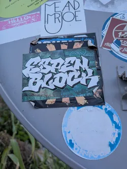 Street sticker A rectangular sticker featuring white, black-outlined graffiti text reading 'ESPEN BLOCK' over a dark green textured background. It is layered on top of another peeling sticker.