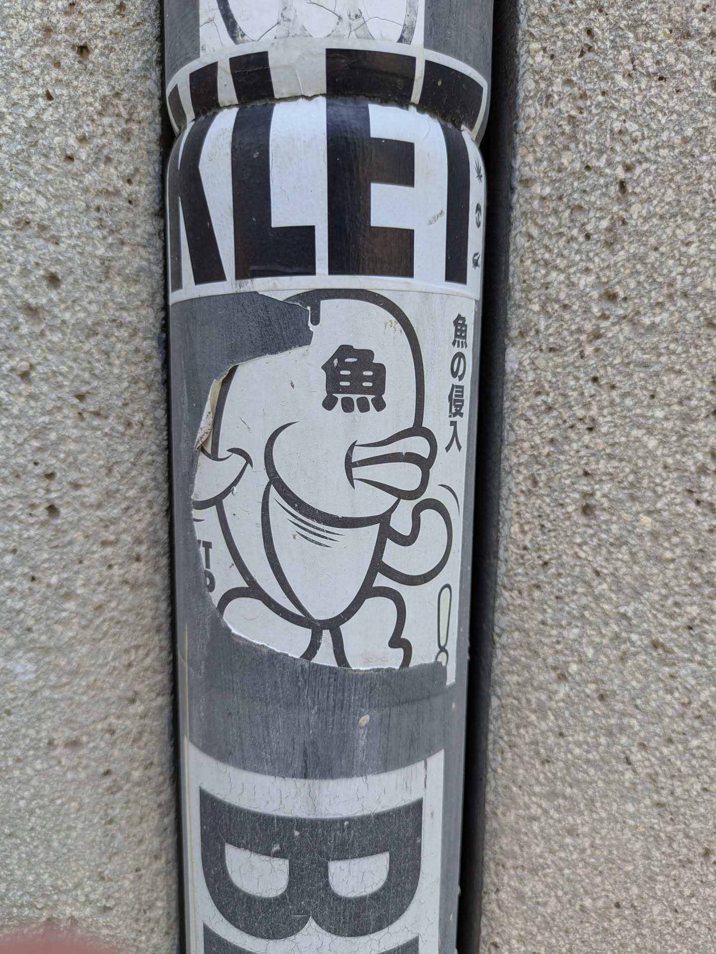 This sticker depicts a cute, rounded fish character with cartoonish features. The fish is drawn in black and white, and to the right of the fish is the vertical Japanese text "魚の侵入" (sakana no shinnyū) which translates to "fish intrusion". The sticker is slightly damaged, with some parts torn off at the edges.