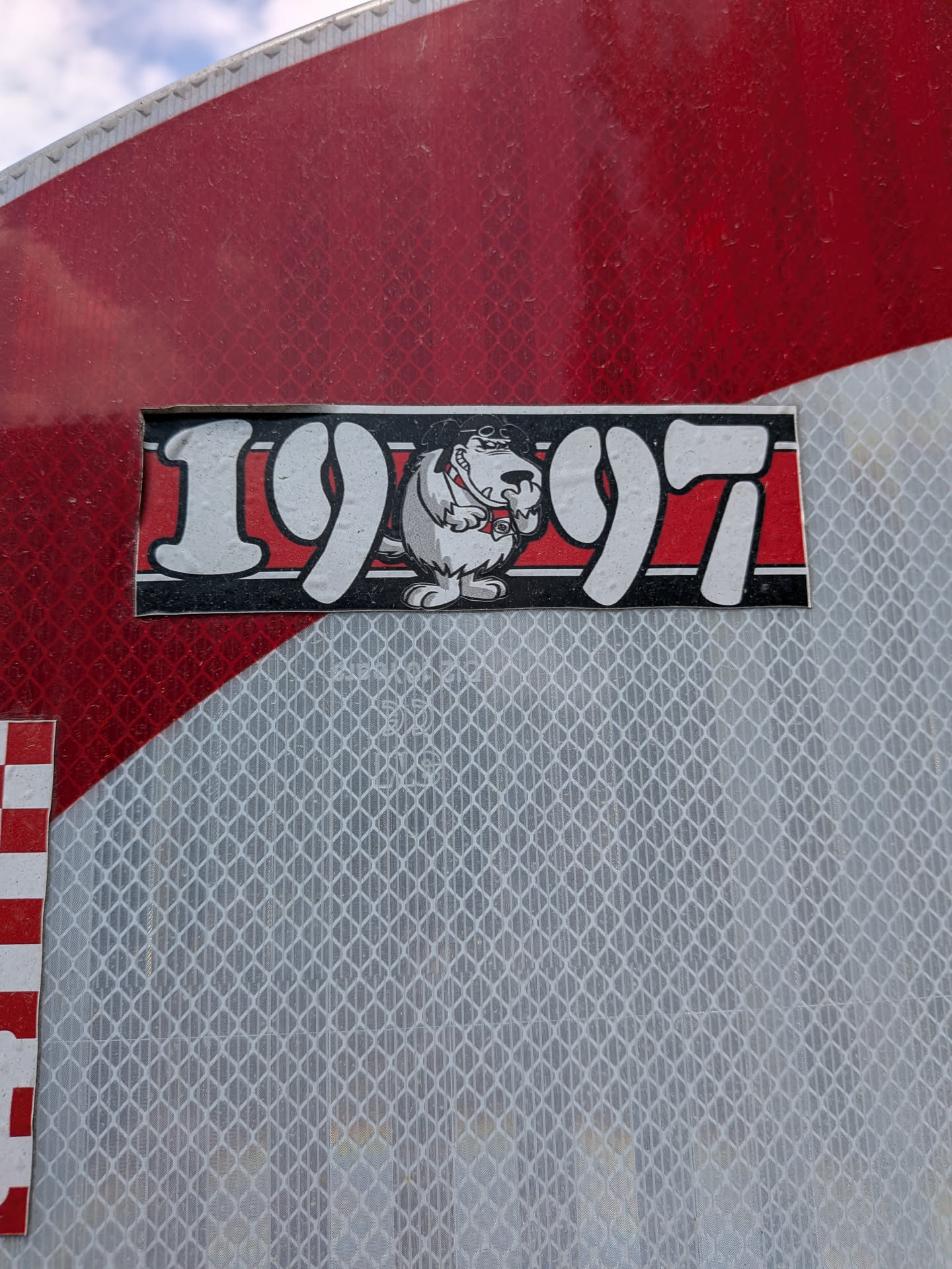 A rectangular black and red sticker featuring the stylized white numbers '19' and '97' flanking a cartoon illustration of the snickering dog Muttley in the center.