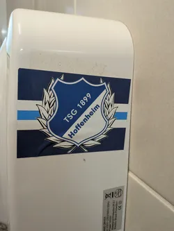 Street sticker A rectangular sticker displaying the TSG 1899 Hoffenheim crest. The blue and white shield is framed by a white laurel wreath, positioned over a background of horizontal dark blue, light blue, and white stripes.