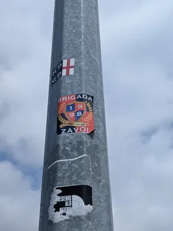 Street sticker Rectangular sticker with a red and black background. Features a central blue and red shield displaying '1998', surrounded by a gold laurel wreath. Text reads 'BRIGADA' at the top and 'ZAVOI' at the bottom.