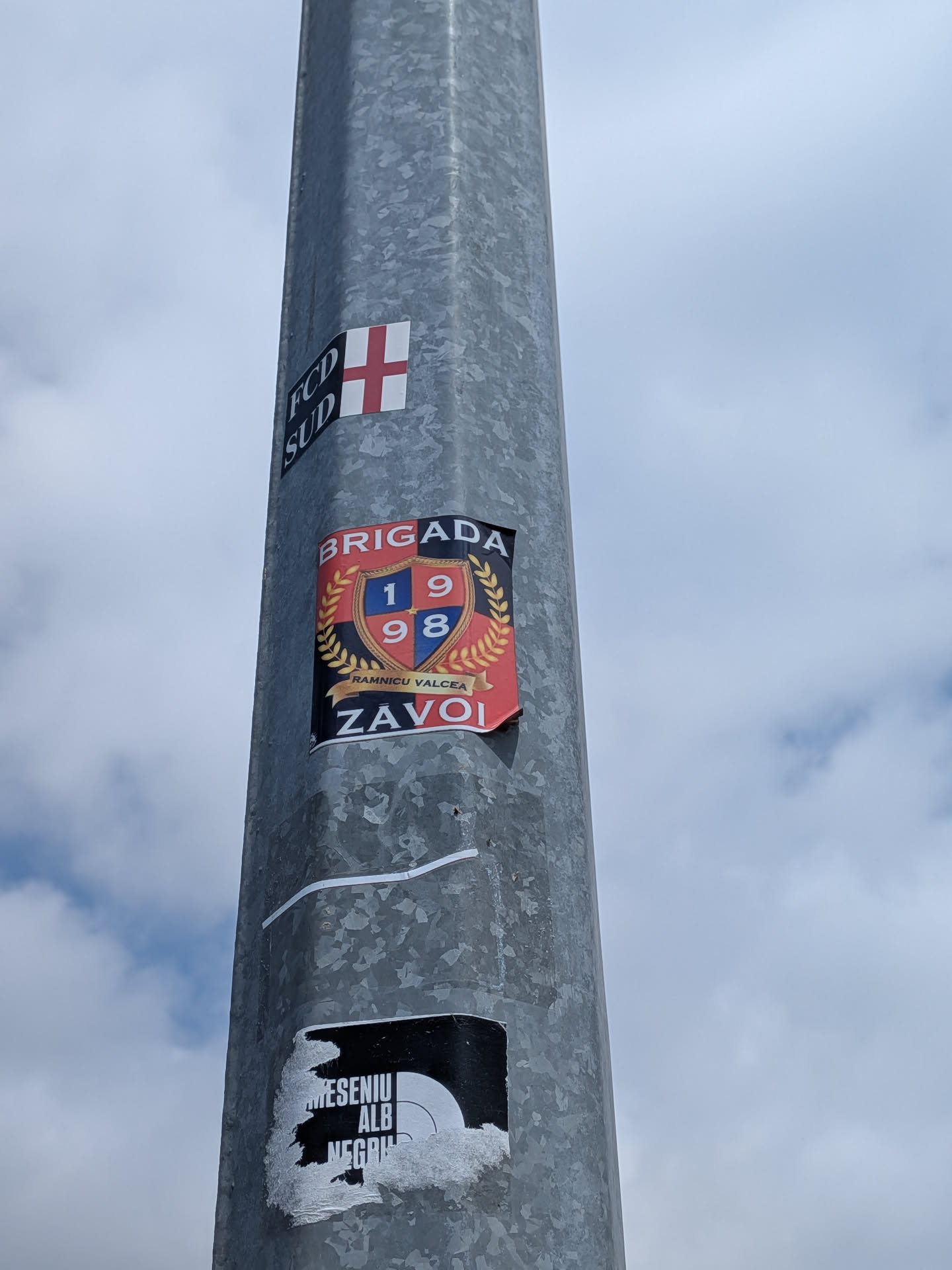 Rectangular sticker with a red and black background. Features a central blue and red shield displaying '1998', surrounded by a gold laurel wreath. Text reads 'BRIGADA' at the top and 'ZAVOI' at the bottom.