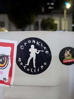 A round black sticker featuring a white silhouette of a violinist in the center. The stylized white text 'Cronkite' curves along the top edge, and 'Satellite' curves along the bottom.